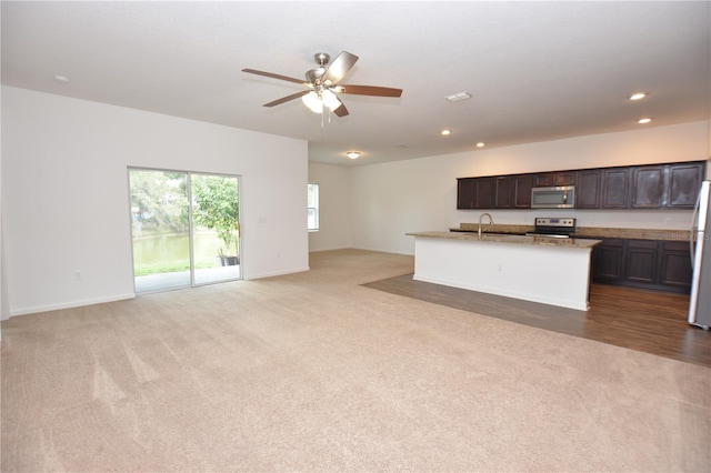 kitchen with carpet floors, a center island with sink, light stone countertops, and appliances with stainless steel finishes