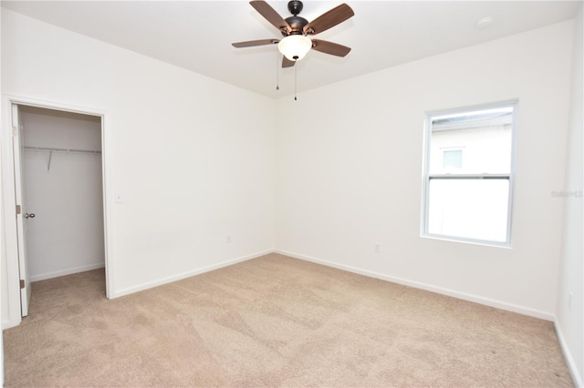 unfurnished bedroom featuring a spacious closet, light carpet, ceiling fan, and a closet