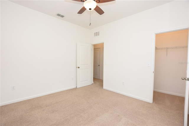 unfurnished bedroom featuring ceiling fan, light colored carpet, a closet, and a walk in closet