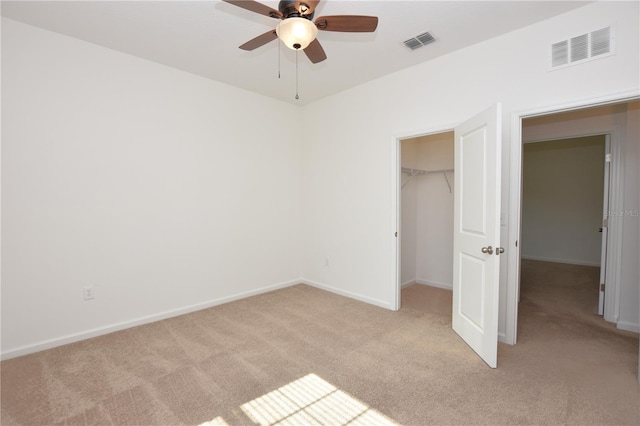 unfurnished bedroom with a walk in closet, light carpet, ceiling fan, and a closet