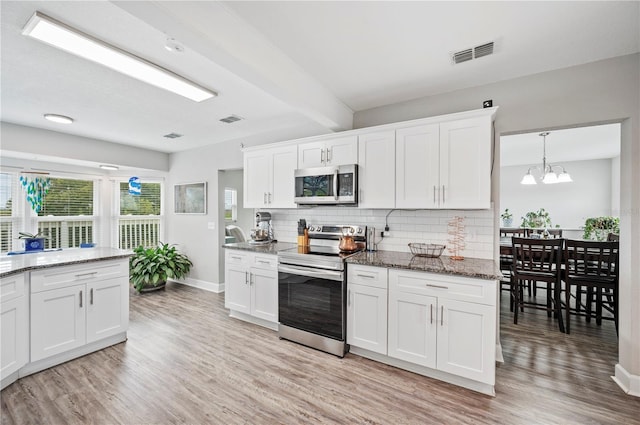 kitchen with appliances with stainless steel finishes, white cabinetry, hanging light fixtures, decorative backsplash, and dark stone counters