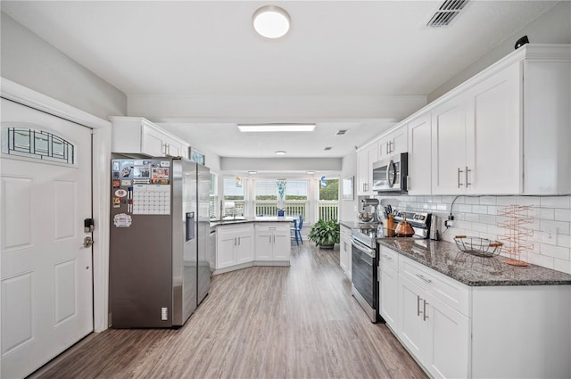 kitchen with dark stone countertops, stainless steel appliances, backsplash, and white cabinets