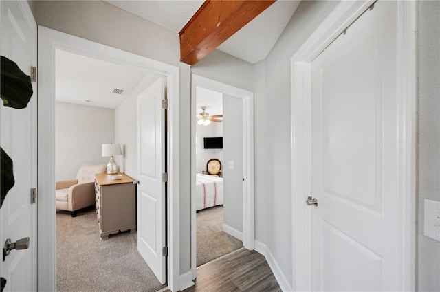 hallway featuring beamed ceiling and light colored carpet