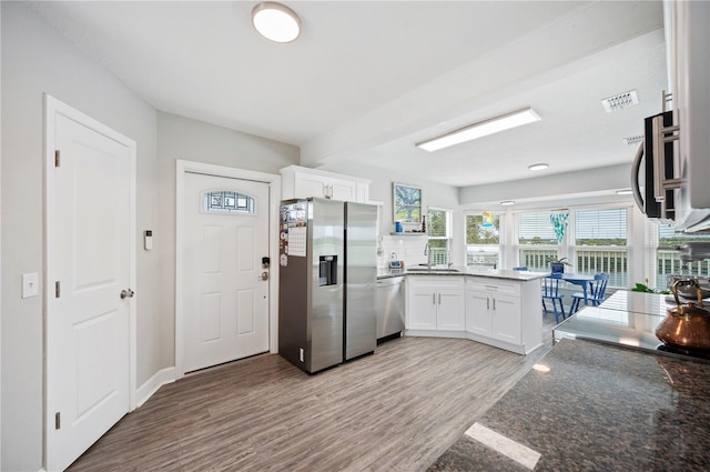 kitchen featuring white cabinetry, wood-type flooring, dark stone countertops, and appliances with stainless steel finishes