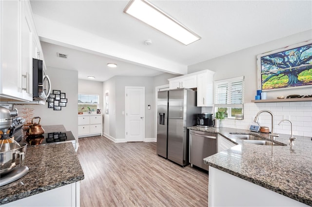 kitchen featuring white cabinets, stainless steel appliances, a sink, dark stone counters, and tasteful backsplash