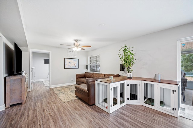 living room featuring wood finished floors, baseboards, and ceiling fan