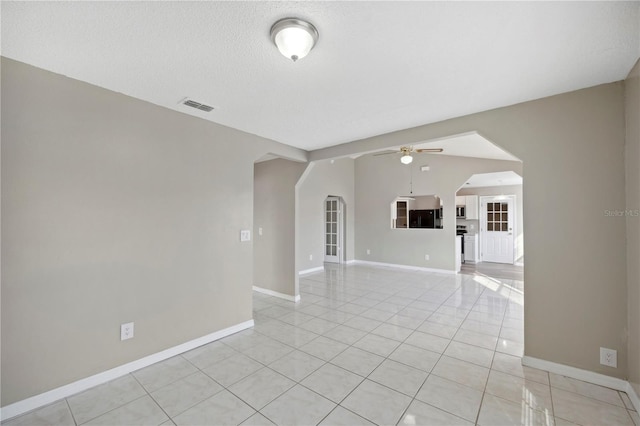 empty room with a textured ceiling, vaulted ceiling, ceiling fan, and light tile patterned flooring