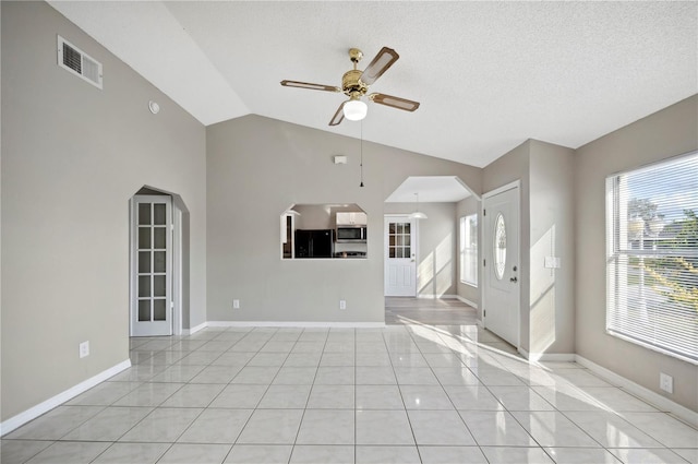 unfurnished living room with vaulted ceiling, light tile patterned floors, a textured ceiling, and ceiling fan