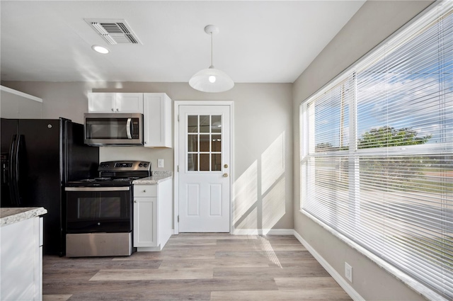 kitchen with appliances with stainless steel finishes, white cabinets, hanging light fixtures, light stone countertops, and light hardwood / wood-style flooring