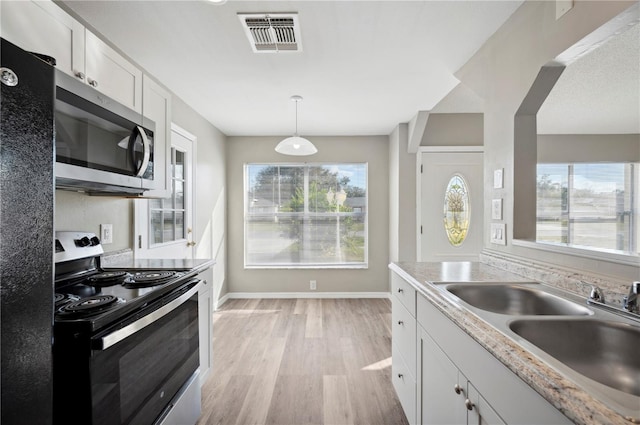 kitchen with appliances with stainless steel finishes, white cabinetry, sink, hanging light fixtures, and light hardwood / wood-style floors