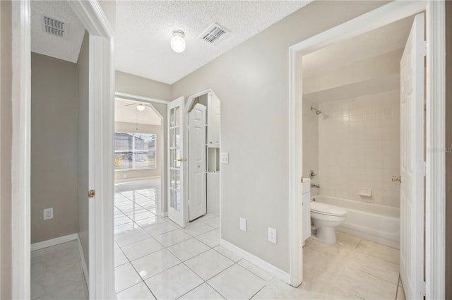 bathroom featuring tiled shower / bath, tile patterned floors, toilet, and a textured ceiling