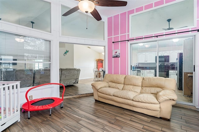 living room with ceiling fan, wood-type flooring, and a high ceiling