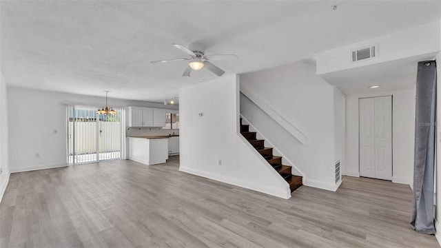 unfurnished living room featuring ceiling fan with notable chandelier and light wood-type flooring