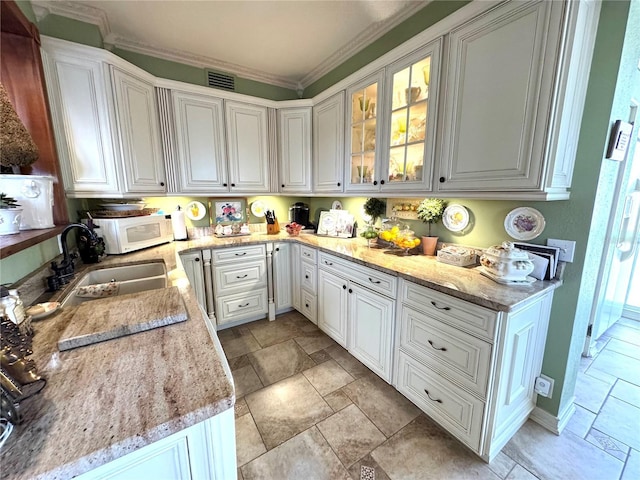 kitchen with white cabinets, white microwave, glass insert cabinets, stone tile flooring, and a sink