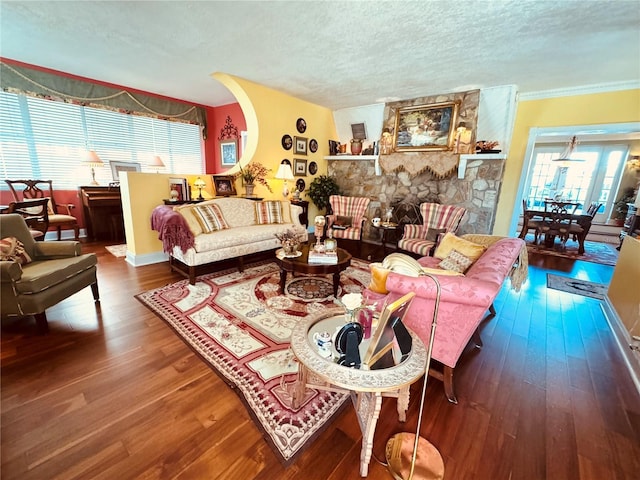 living area featuring ornamental molding, a stone fireplace, a textured ceiling, wood finished floors, and baseboards