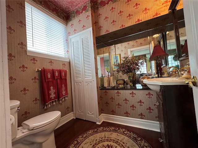 bathroom with toilet, vanity, baseboards, a closet, and wallpapered walls