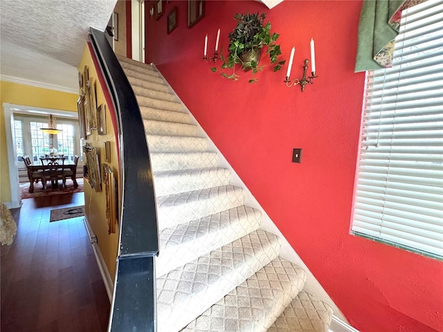 stairs featuring a textured ceiling, a textured wall, ornamental molding, and wood finished floors