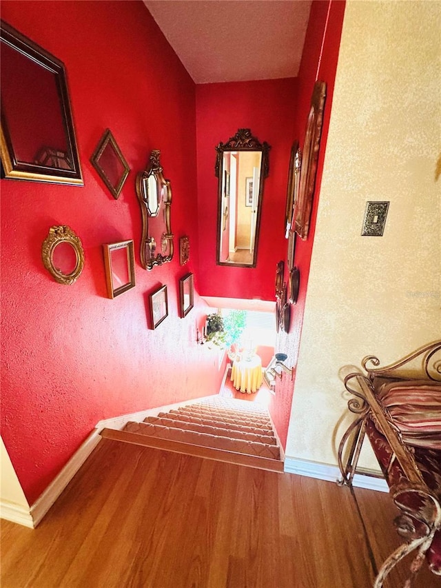 hallway with a textured wall, wood finished floors, and baseboards