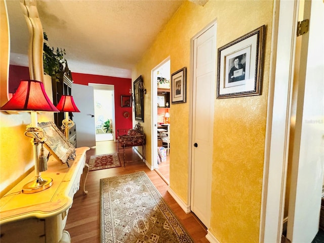 doorway featuring a textured wall, baseboards, and wood finished floors