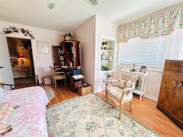 bedroom featuring a textured ceiling, baseboards, and wood finished floors