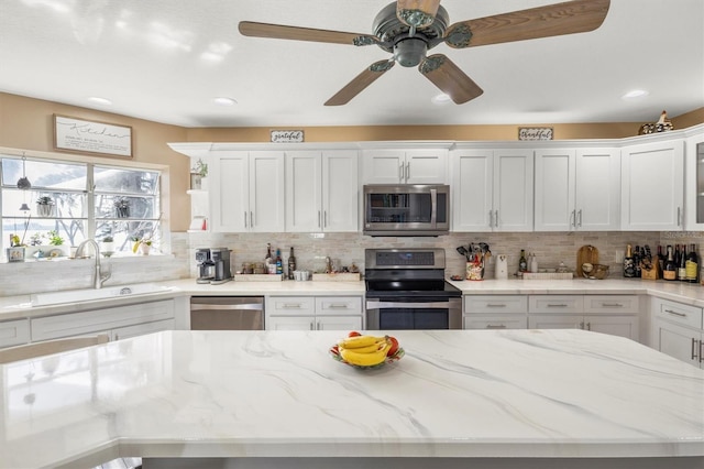kitchen featuring tasteful backsplash, light stone counters, white cabinets, stainless steel appliances, and a sink