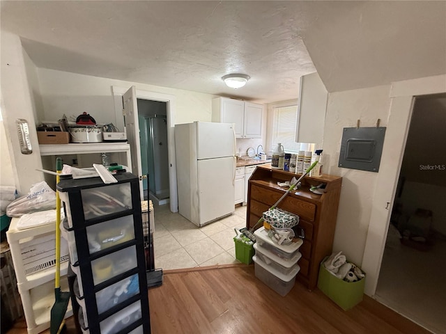 kitchen featuring a textured ceiling, light wood-type flooring, electric panel, white fridge, and white cabinets