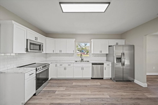 kitchen with stainless steel appliances, white cabinetry, sink, and light hardwood / wood-style flooring