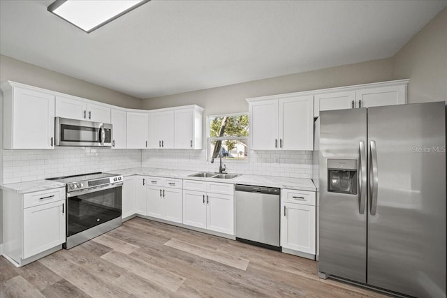 kitchen with sink, white cabinetry, light stone counters, light wood-type flooring, and stainless steel appliances