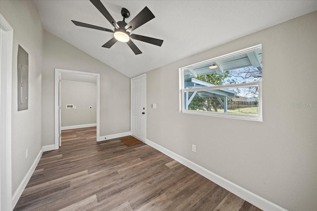 empty room with dark hardwood / wood-style flooring, vaulted ceiling, electric panel, and ceiling fan