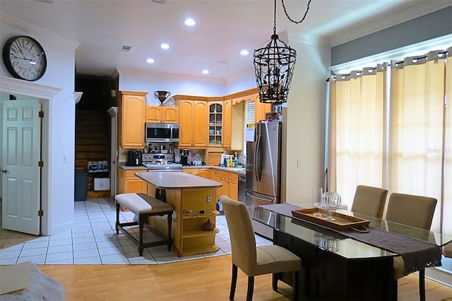 kitchen with decorative light fixtures, light tile patterned floors, ornamental molding, a kitchen island, and stainless steel appliances