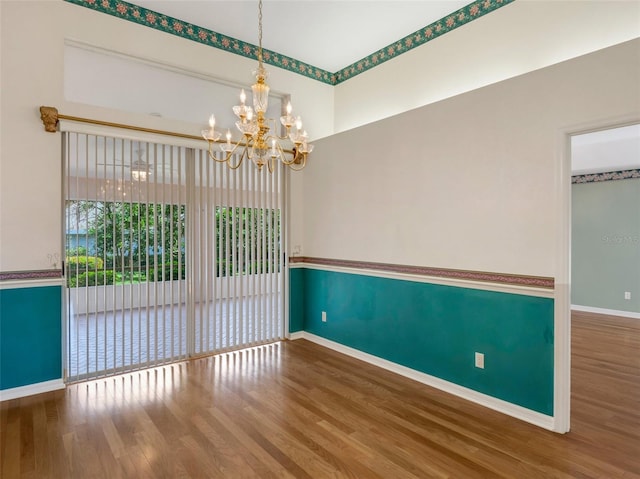 empty room with hardwood / wood-style flooring and an inviting chandelier