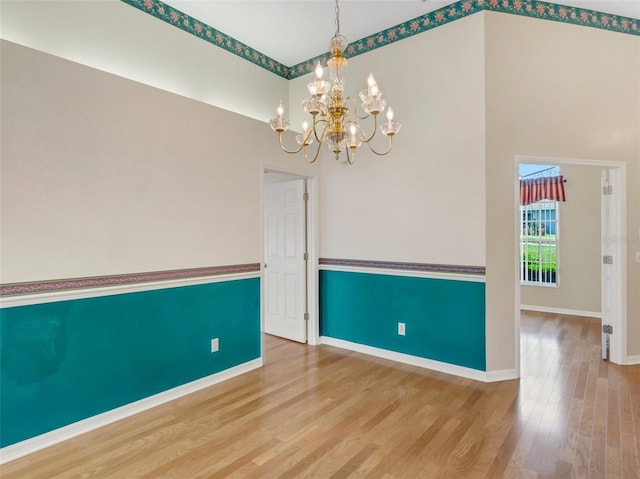 unfurnished room featuring a high ceiling, wood-type flooring, and a chandelier