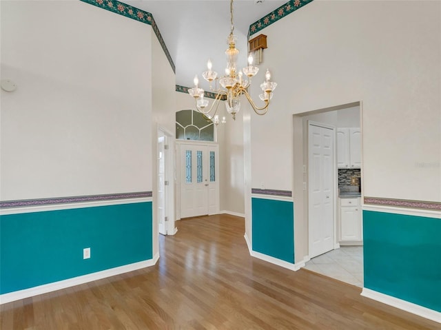 unfurnished dining area with an inviting chandelier, light hardwood / wood-style floors, and a high ceiling