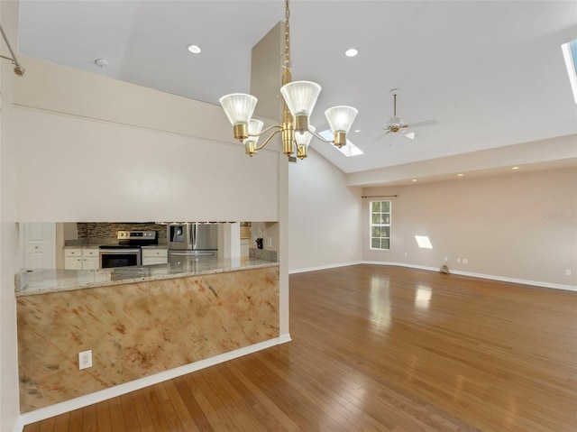 kitchen featuring lofted ceiling, appliances with stainless steel finishes, hanging light fixtures, light stone counters, and dark hardwood / wood-style flooring