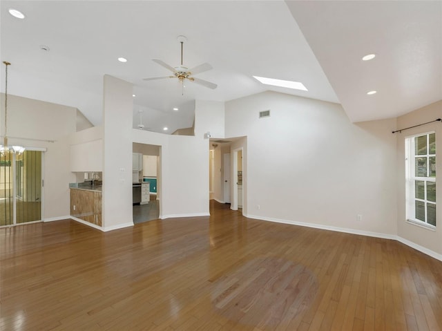 unfurnished living room with ceiling fan with notable chandelier, dark hardwood / wood-style floors, a skylight, and high vaulted ceiling