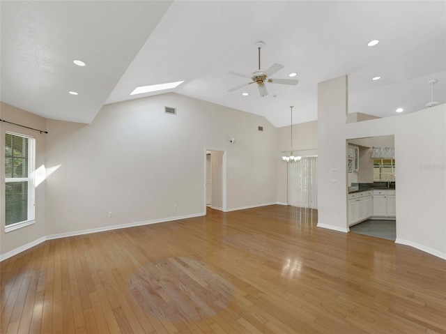 unfurnished living room featuring hardwood / wood-style flooring, ceiling fan with notable chandelier, and high vaulted ceiling