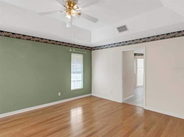 unfurnished room featuring a tray ceiling, light hardwood / wood-style flooring, and ceiling fan