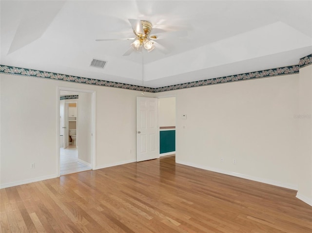 spare room with ceiling fan, a raised ceiling, and light wood-type flooring