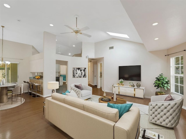 living room featuring wood-type flooring, ceiling fan with notable chandelier, high vaulted ceiling, and a skylight