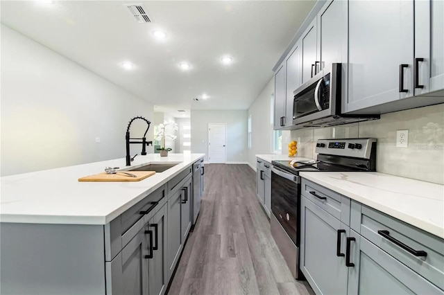 kitchen with tasteful backsplash, gray cabinetry, light wood-style flooring, stainless steel appliances, and a sink