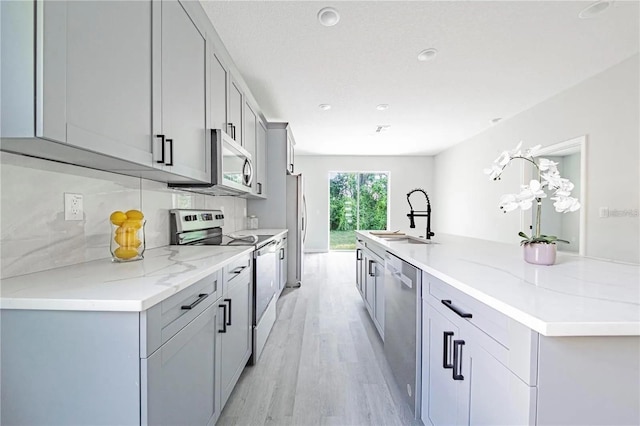 kitchen with light wood finished floors, tasteful backsplash, a large island with sink, appliances with stainless steel finishes, and a sink