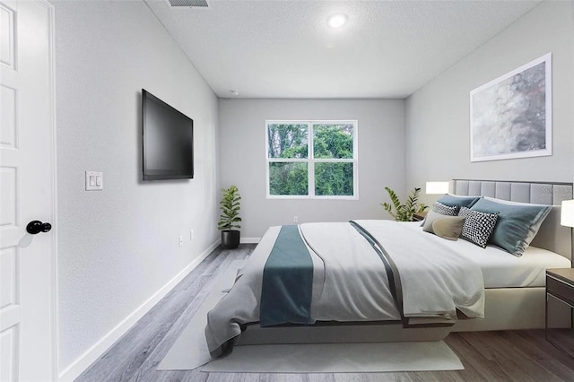 bedroom featuring visible vents, a textured ceiling, baseboards, and wood finished floors