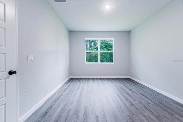 spare room featuring visible vents, baseboards, a textured ceiling, and wood finished floors