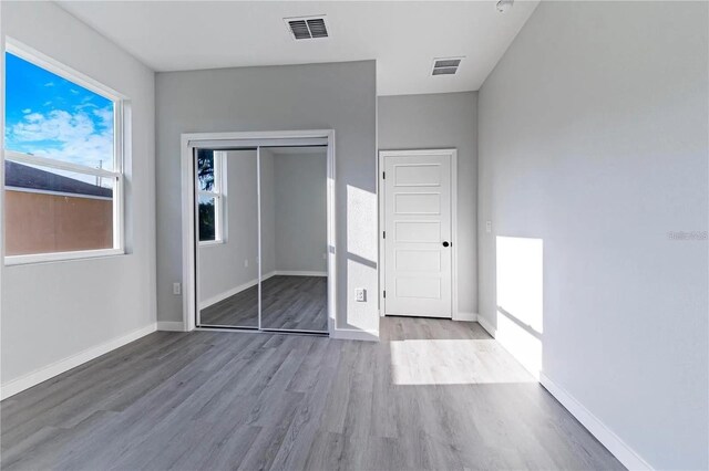 unfurnished bedroom featuring a closet, visible vents, baseboards, and wood finished floors