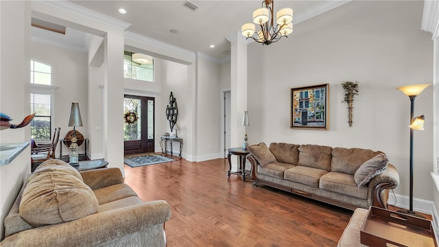 living room featuring a towering ceiling, ornamental molding, a chandelier, and hardwood / wood-style floors