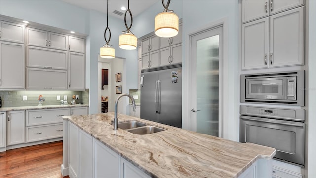 kitchen with sink, tasteful backsplash, light stone counters, built in appliances, and hanging light fixtures