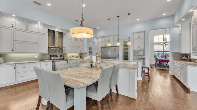 kitchen with a spacious island, white cabinets, stainless steel appliances, and wall chimney range hood