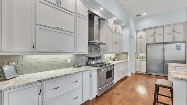 kitchen featuring white cabinetry, a breakfast bar area, premium appliances, light hardwood / wood-style floors, and wall chimney range hood