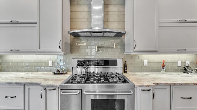 kitchen featuring gas stove, white cabinetry, tasteful backsplash, light stone countertops, and wall chimney range hood