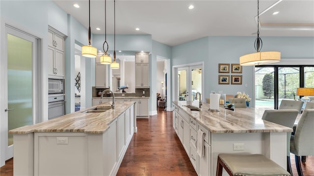 kitchen with a spacious island, sink, light stone counters, decorative light fixtures, and stainless steel microwave